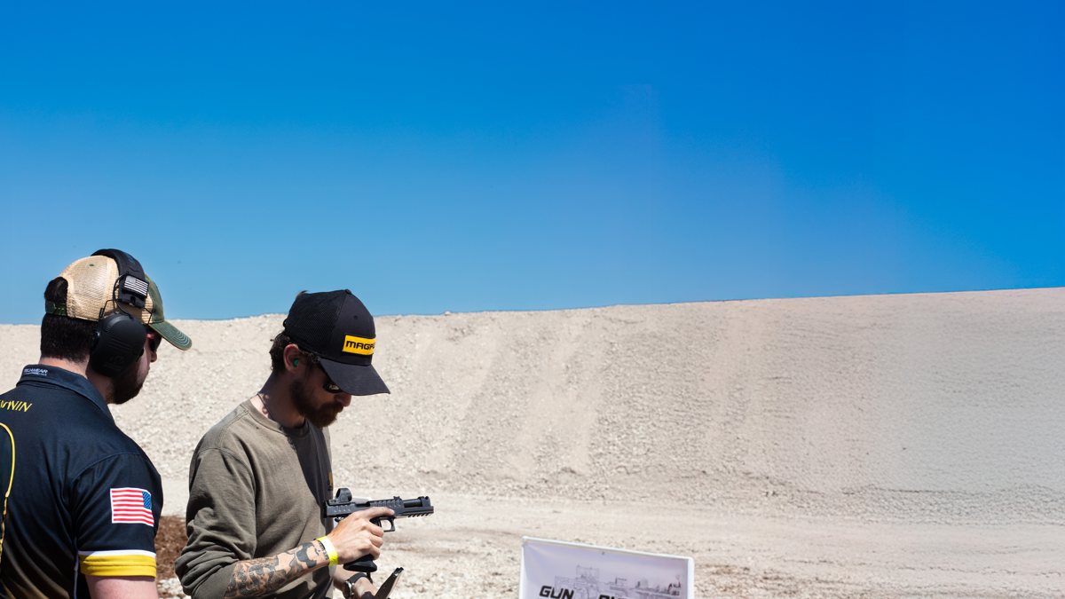 Shooter handling a Watchtower Defense pistol with a red dot at an outdoor range event